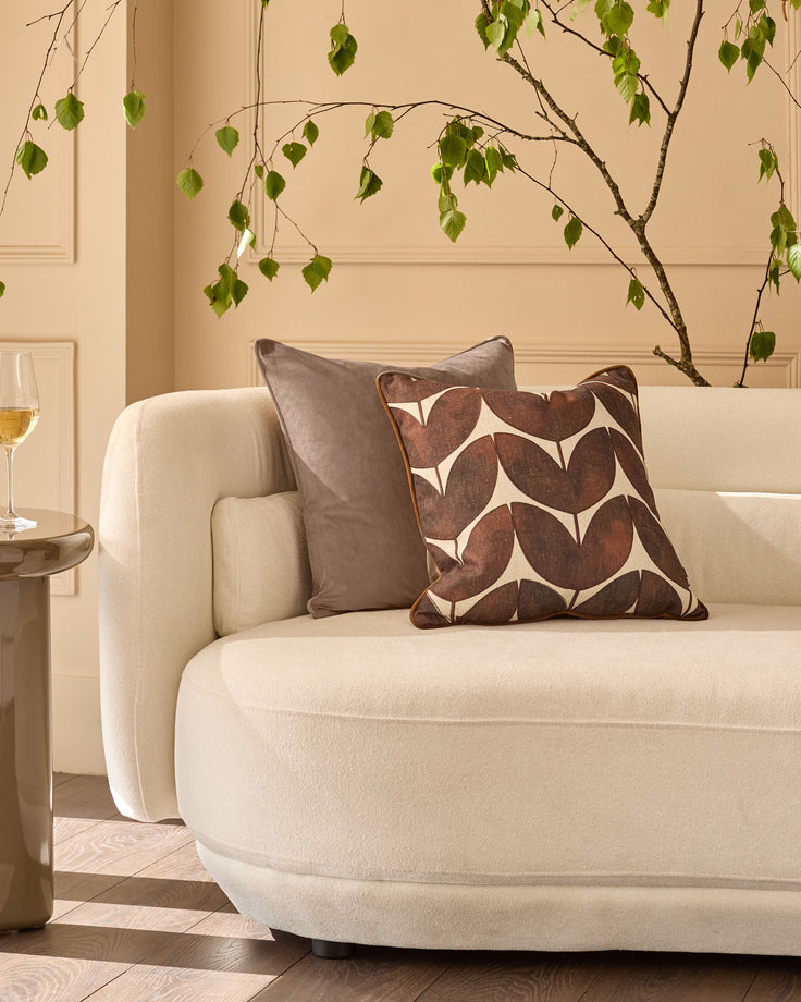 Luca cushion in mink displayed on a cream armchair, featuring a geometric leaf pattern in brown and cream tones.