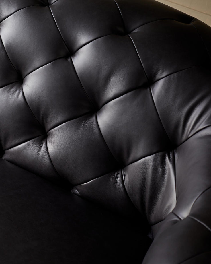 Close-up of a luxurious, button-tufted black leather chair, showcasing its plush texture and elegant design.