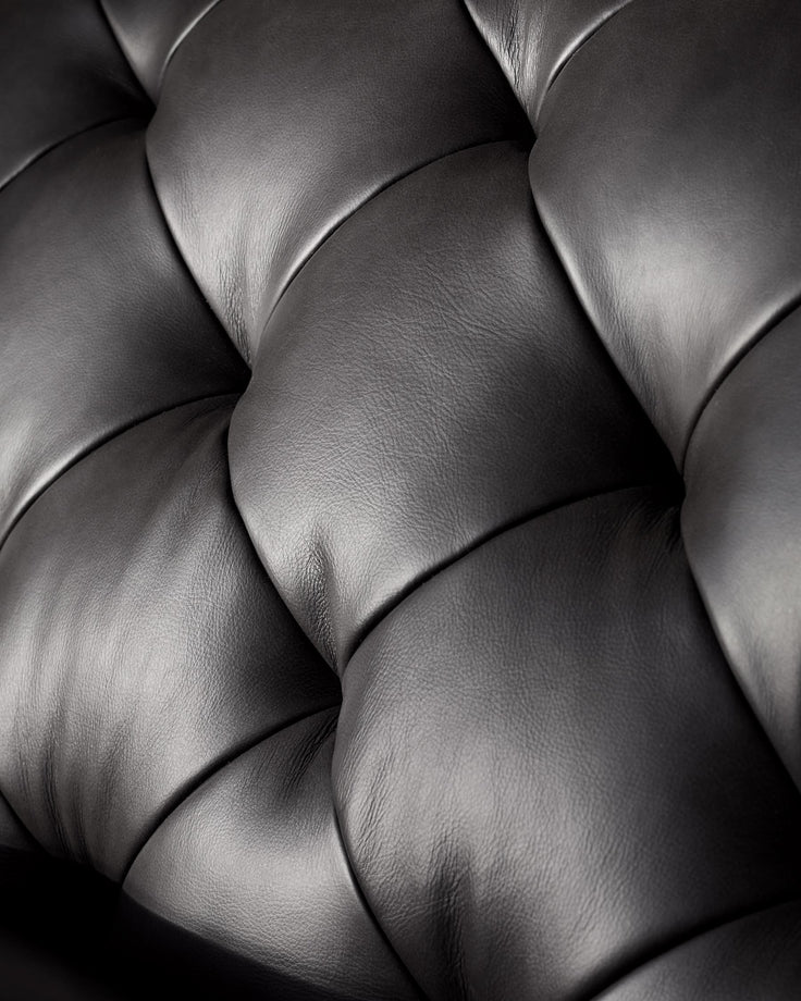 Close-up of a luxurious, deep-buttoned, black leather sofa, showcasing its intricate design and soft texture.
