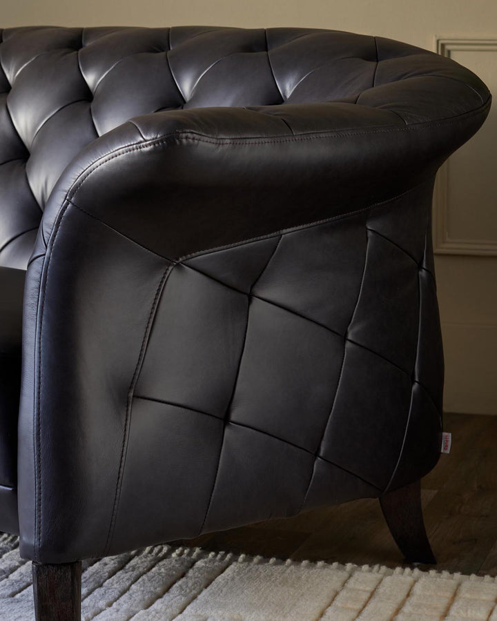 Close-up of a stylish black leather Chesterfield sofa with a tufted design and elegant wooden legs.