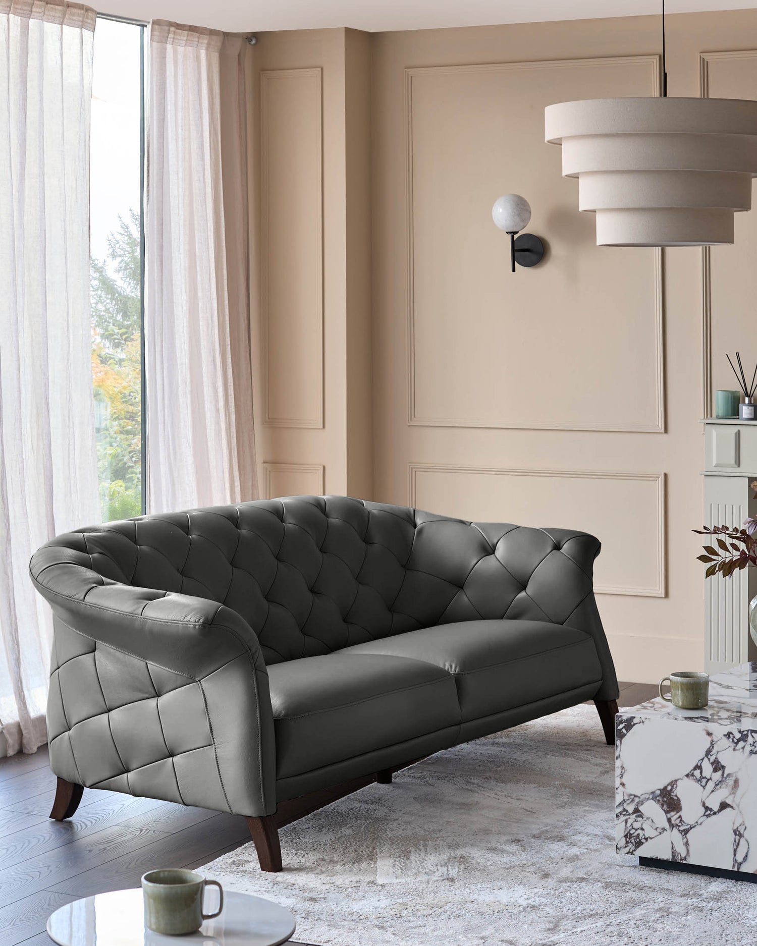 A grey leather sofa with buttoned detailing sits on a patterned rug in a room with neutral tones.