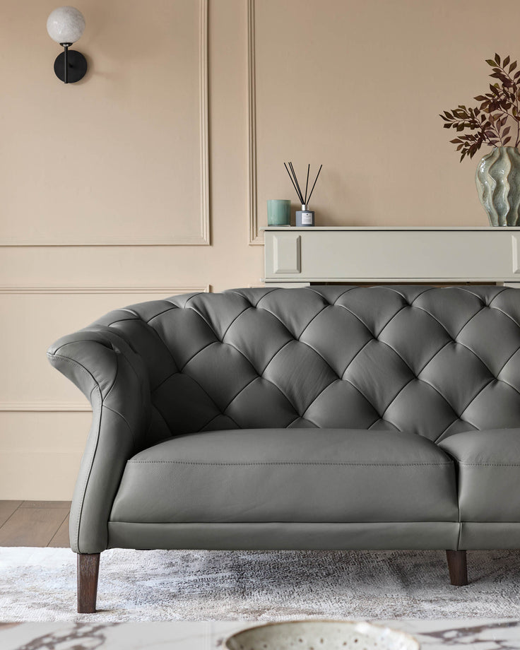 Elegant grey leather sofa with button detailing and wooden legs, set against a neutral wall.