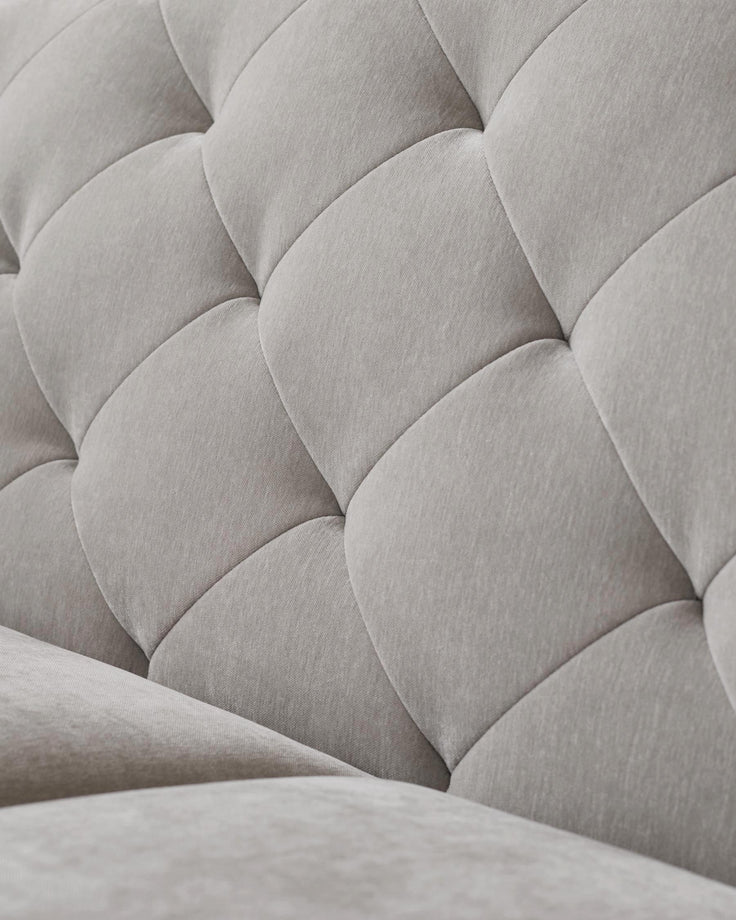 Close-up of a luxurious, button-tufted light grey sofa, showcasing the texture and detailed craftsmanship.