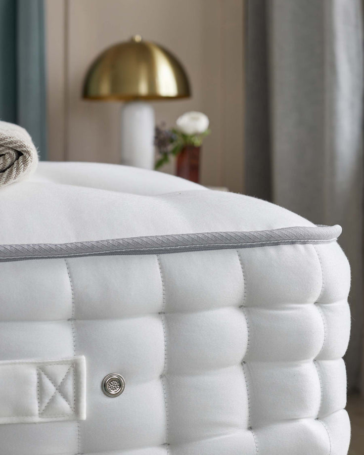 Close-up of a luxurious, quilted mattress with grey piping and button detailing, showcasing its premium comfort and design.