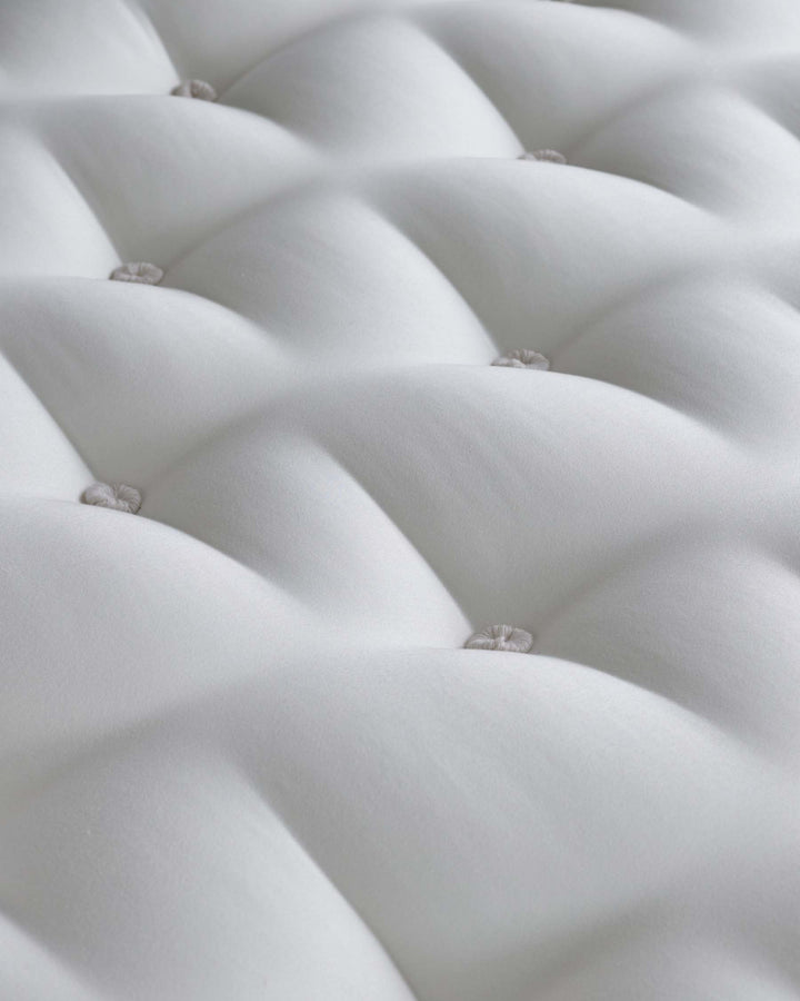 Close-up of a white, tufted mattress. Soft texture and rounded cushions provide a comfortable and luxurious sleep surface.