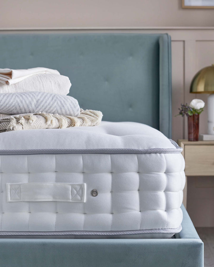 Close-up of a mattress on a blue bed frame, complete with folded blankets and bedside furniture.