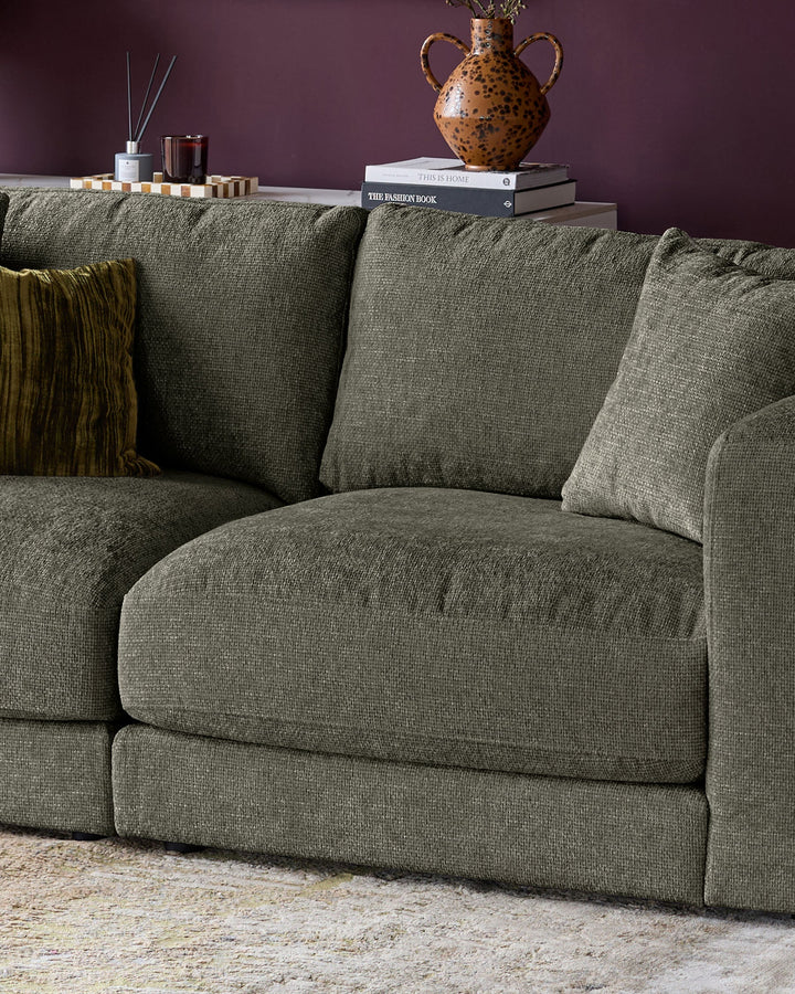 Lynetta 3-seater sofa in dark green weave fabric, styled with cushions and a throw, against a purple wall.