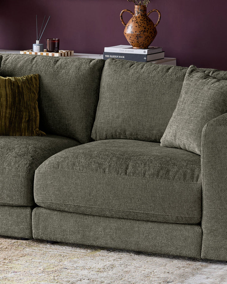 Lynetta 3-seater sofa in dark green weave fabric, styled with cushions and a throw, against a purple wall.