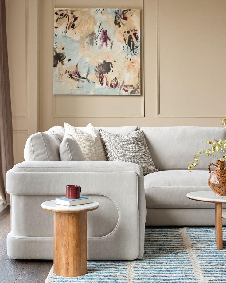 Lynetta small corner sofa in natural grey weave fabric, styled in a bright living room with wooden side tables and decorative pillows.