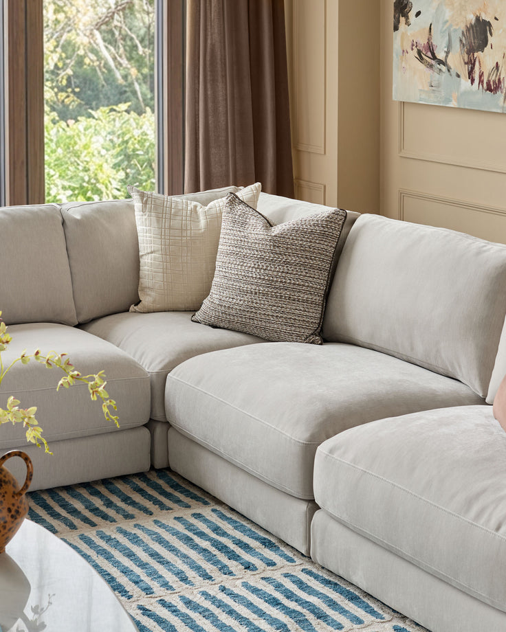 Lynetta small corner sofa in natural grey weave fabric, styled with patterned pillows in a bright living room setting.