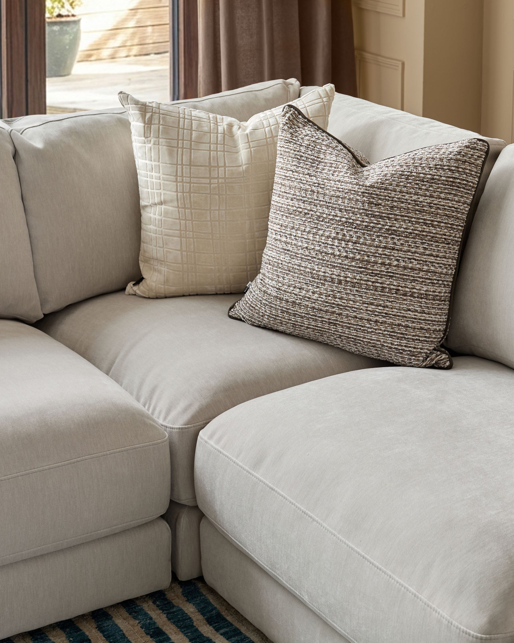 Lynetta small corner sofa in natural grey weave fabric with decorative throw pillows, angled room view.