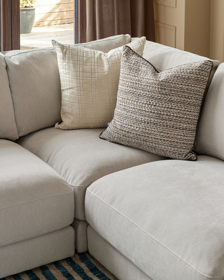 Lynetta small corner sofa in natural grey weave fabric with decorative throw pillows, angled room view.