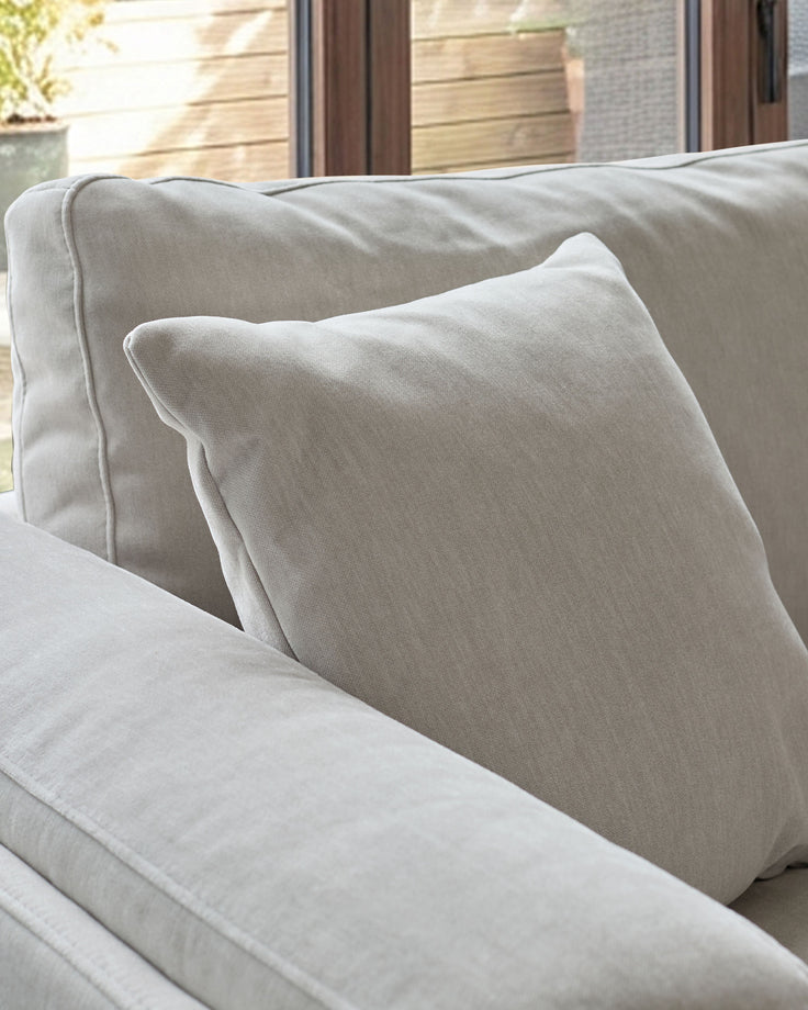 Light grey upholstered corner sofa with rolled arms and matching cushion, natural weave fabric finish.