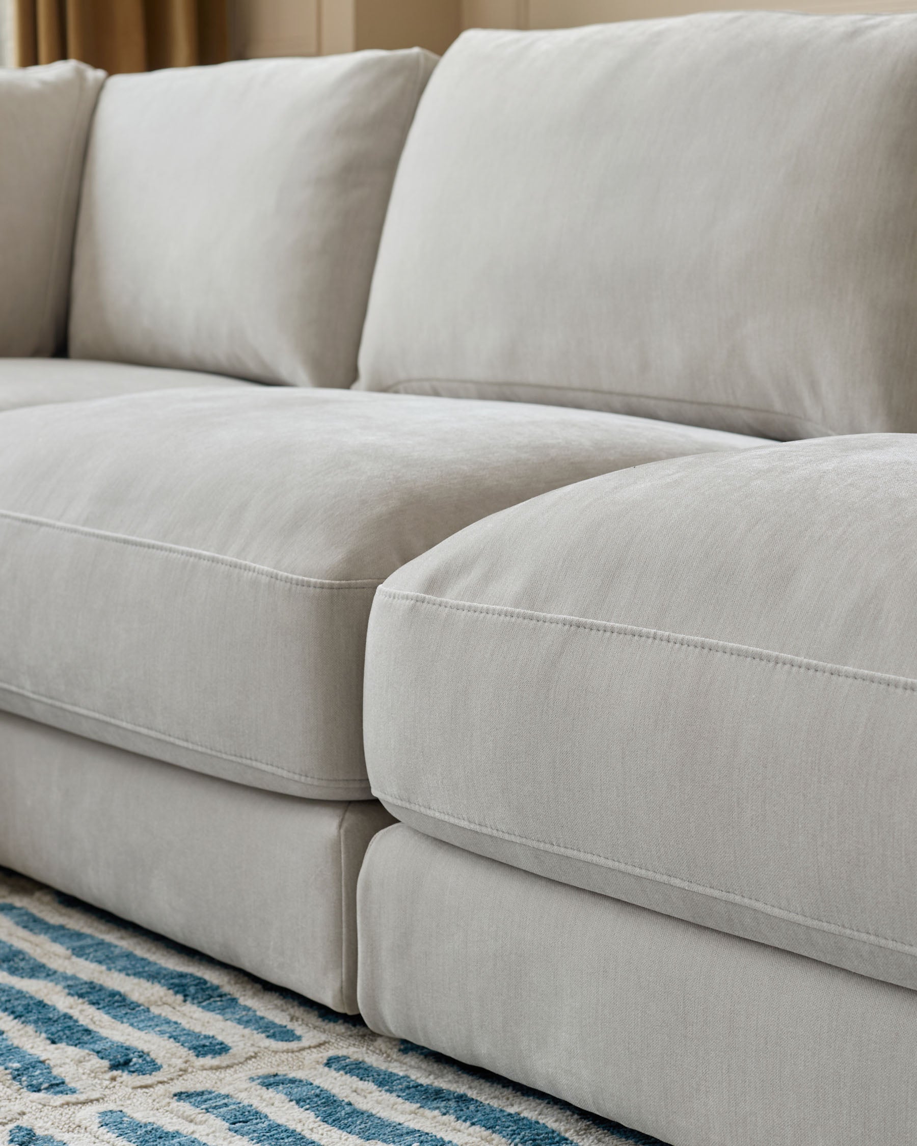 Lynetta small corner sofa in natural grey weave fabric, showing plush cushions and curved seating detail with patterned rug.