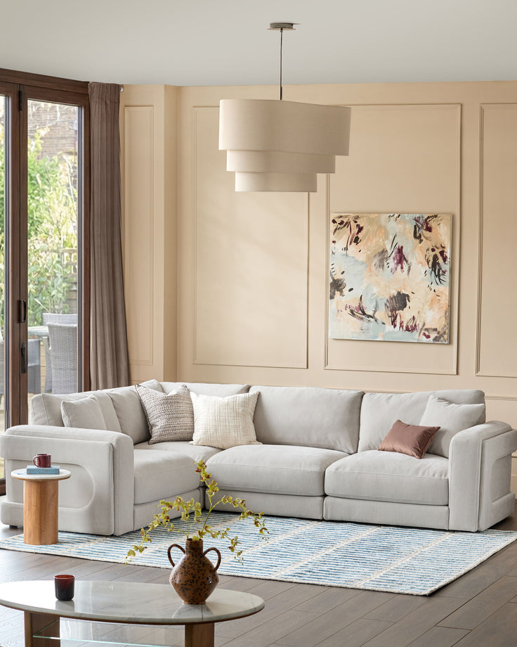Burleigh 2-bulb pendant light in natural linen, shown hanging above a sectional sofa in a cream living room.