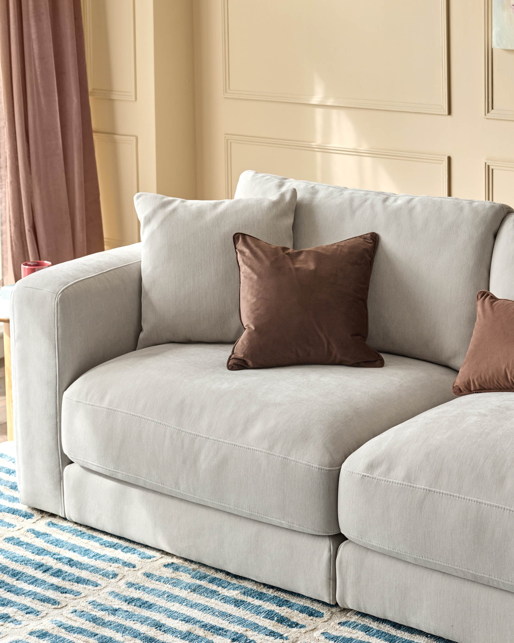 Lynetta 3-seater sofa in natural grey weave fabric with rounded arms and brown accent pillows in a styled room setting.