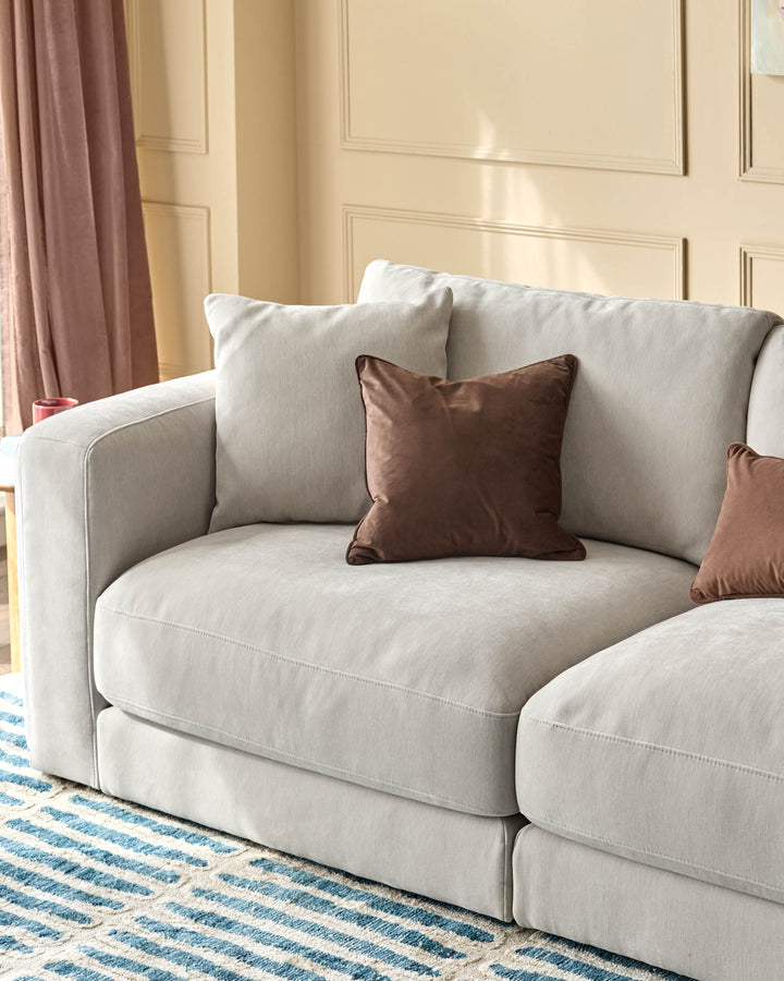 Lynetta 3-seater sofa in natural grey weave fabric with rounded arms and brown accent pillows in a styled room setting.