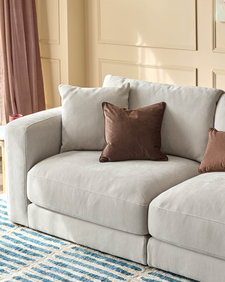 Lynetta 3-seater sofa in natural grey weave fabric with rounded arms and brown accent pillows in a styled room setting.