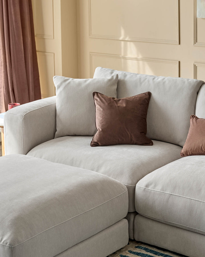 Lynetta 3-seater sofa with footstool in natural grey weave fabric, curved design with brown accent pillows in modern room setting.