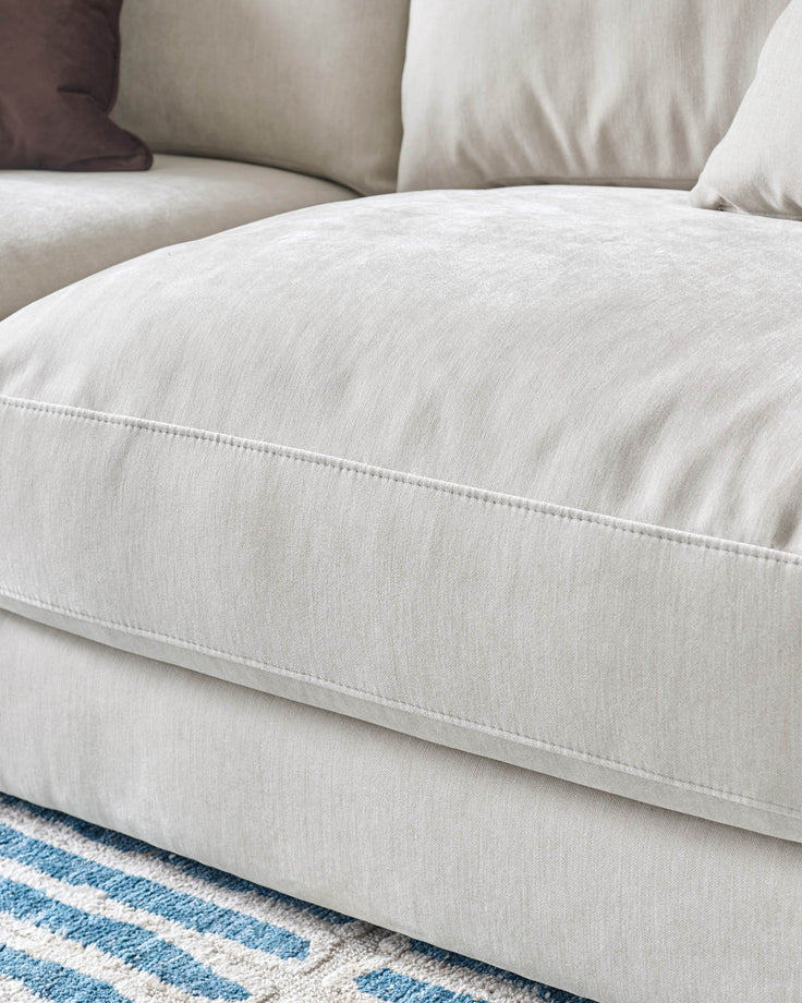 Cream linen 3-seater sofa with cushioned armrest and piping detail, positioned on blue striped rug.