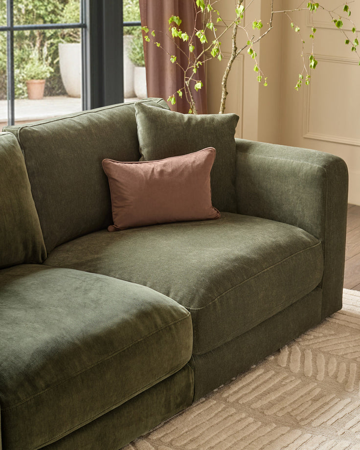 Lynetta 3-seater sofa in dark green weave fabric, angled view with decorative pillows and trailing plants in background.