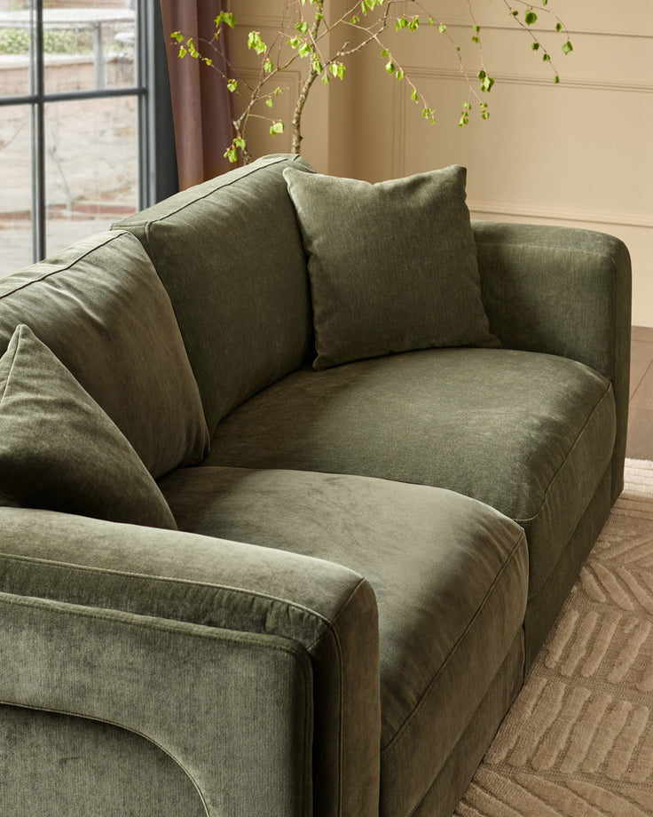 Lynetta 3-seater sofa in dark green weave fabric, curved armrests, decorative pillows, angled view near window.