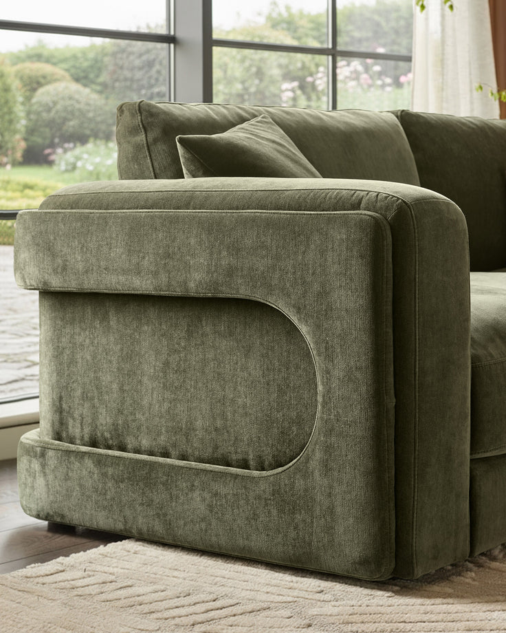 Lynetta 3-seater sofa with footstool in dark green weave fabric, shown from side angle near large windows with garden view.
