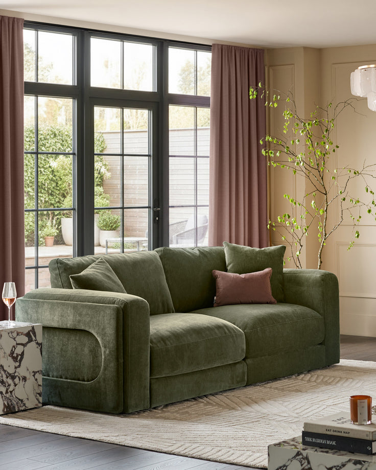Lynetta 3-seater sofa in dark green weave fabric, positioned in a bright living room with large windows and mauve curtains.