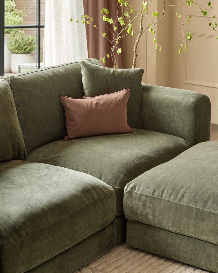 Lynetta 3-seater sofa with footstool in dark green weave fabric, styled with burgundy and sage cushions in a bright room.