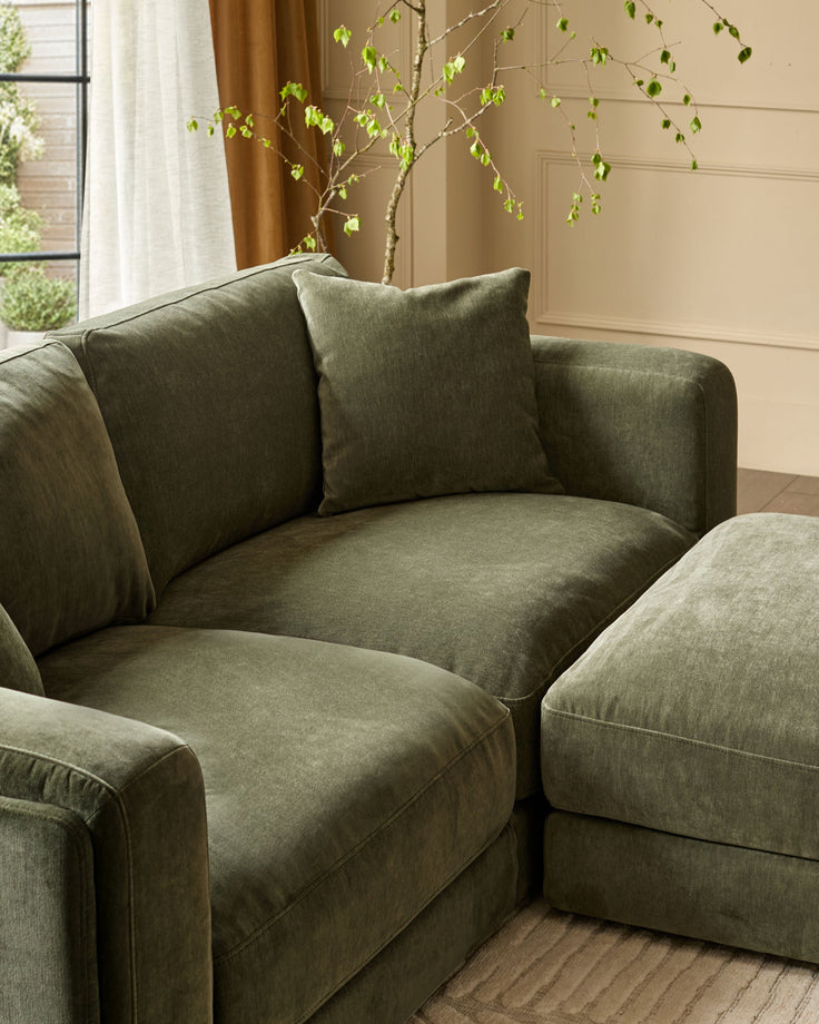 Dark green weave fabric 3-seater sofa with footstool, curved design, decorative pillow, styled living room setting.