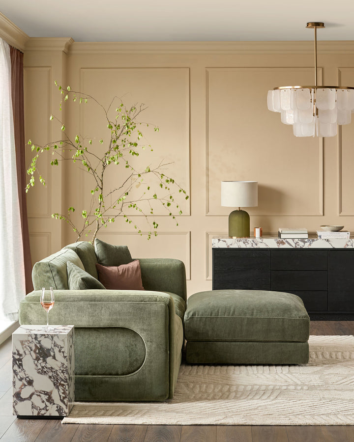 Dark green Lynetta 3-seater sofa with matching footstool in a beige living room setting, showing the sofa's curved design and upholstered weave fabric.