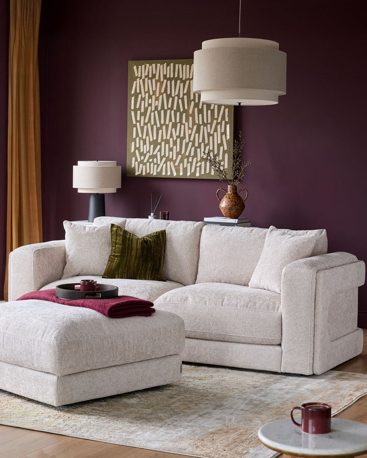 Lynetta 3-seater sofa with footstool in natural weave fabric, displayed in a styled living room setting with burgundy walls.