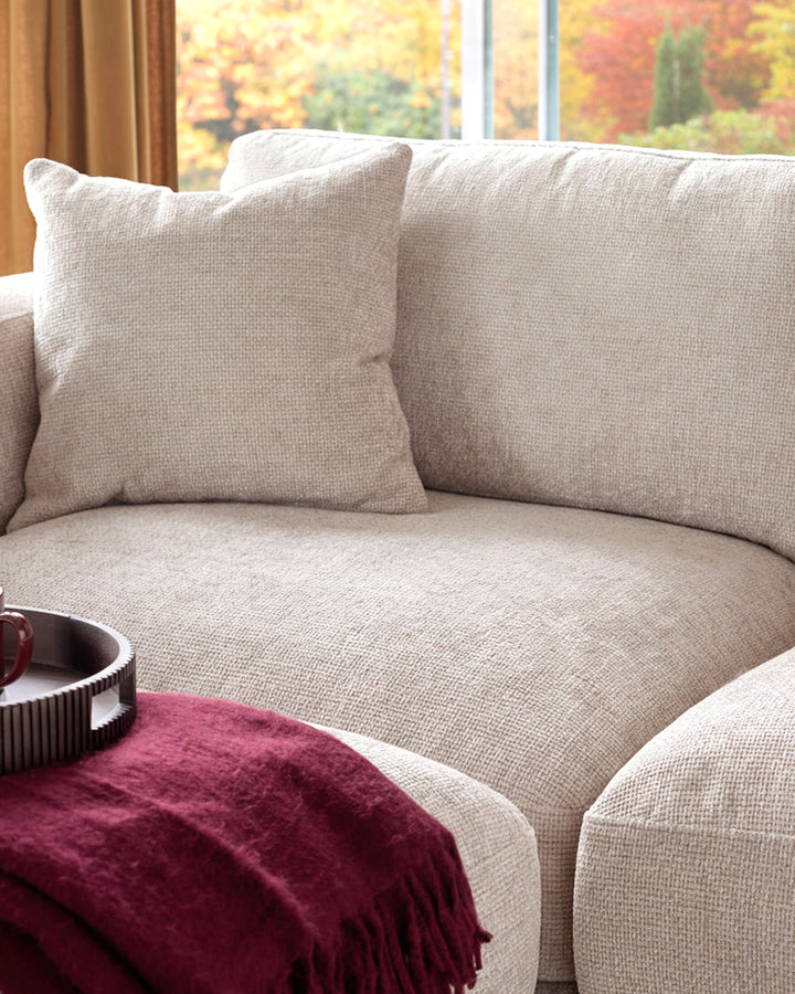 Lynetta 3-seater sofa in natural weave fabric, shown with decorative pillows and burgundy throw blanket by window.
