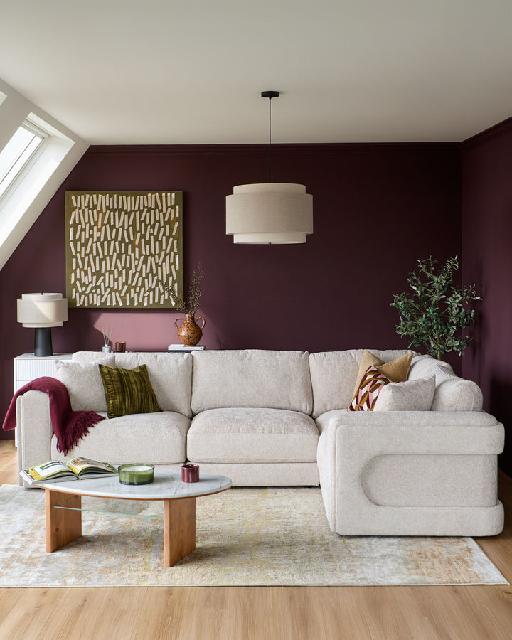 Lynetta small corner sofa in natural weave fabric, displayed in a living room with burgundy walls and wooden coffee table.