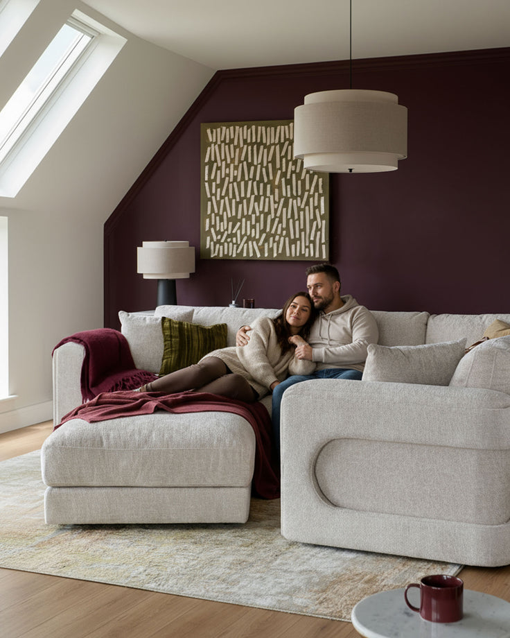 Lynetta small corner sofa with footstool in natural weave fabric, styled in a cozy attic bedroom with burgundy accents.