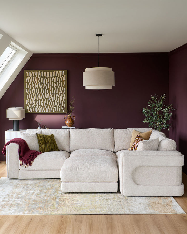 Lynetta small corner sofa with footstool in natural weave fabric, L-shaped configuration in burgundy room setting.