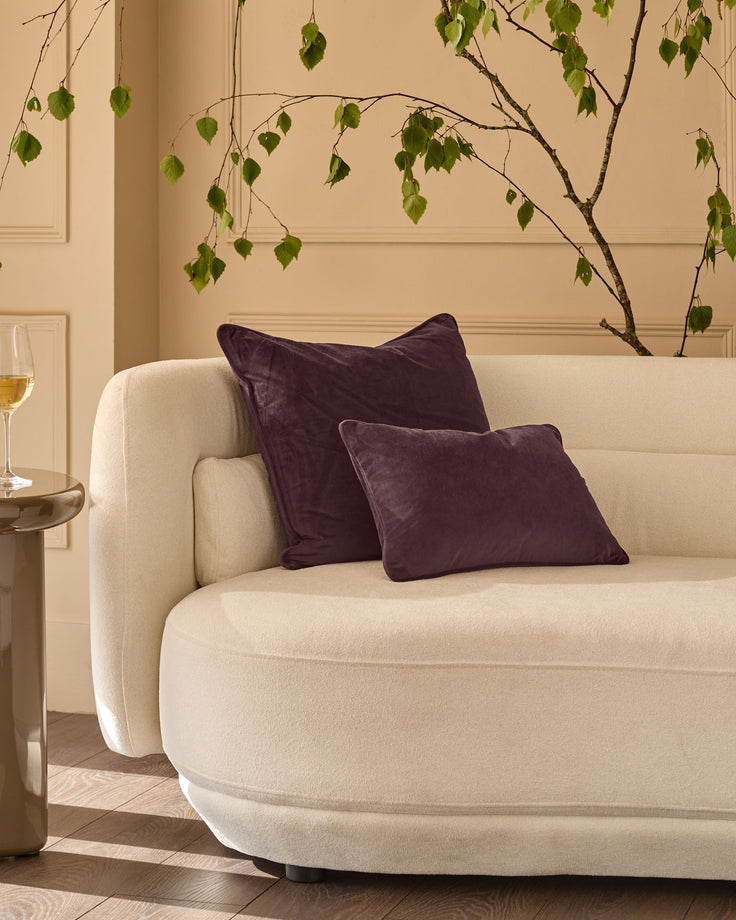 Luca Cushion Large in Mulberry, displayed on a cream armchair in a styled living room setting.