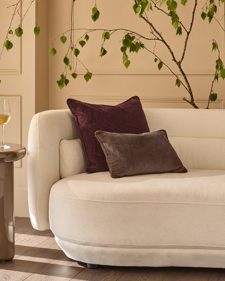 Chocolate velvet rectangular cushion displayed on a cream curved sofa in a styled living room setting.