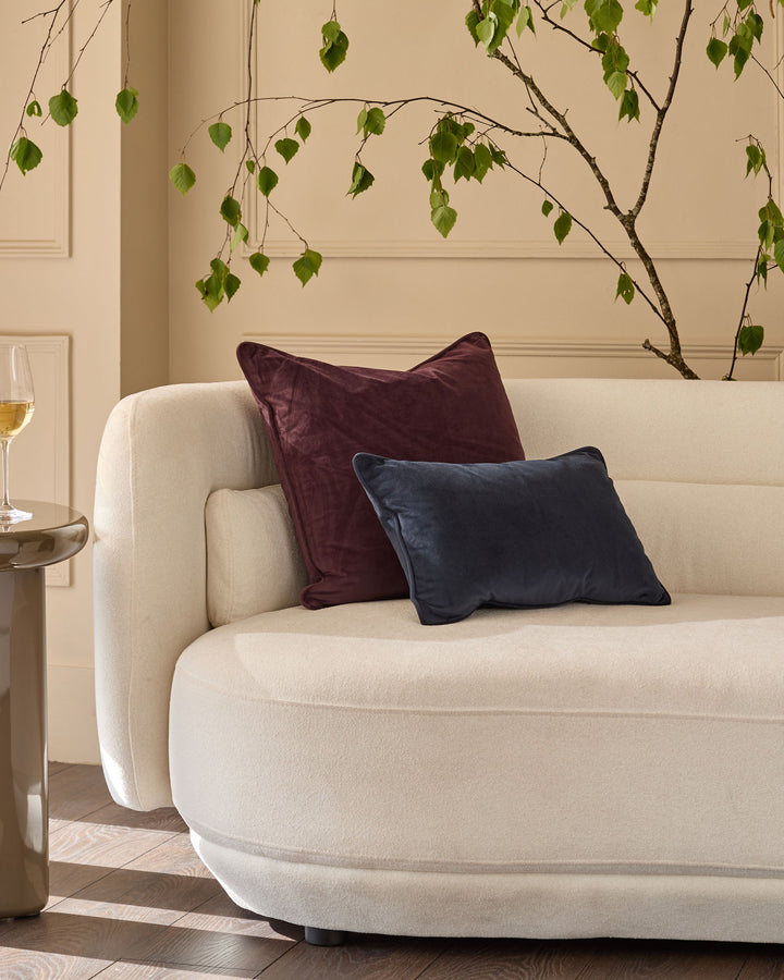 Navy blue rectangular cushion displayed on a cream curved sofa in a modern living room setting.