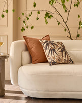 Large rust-colored cushion displayed on a cream upholstered armchair in a styled living room setting.