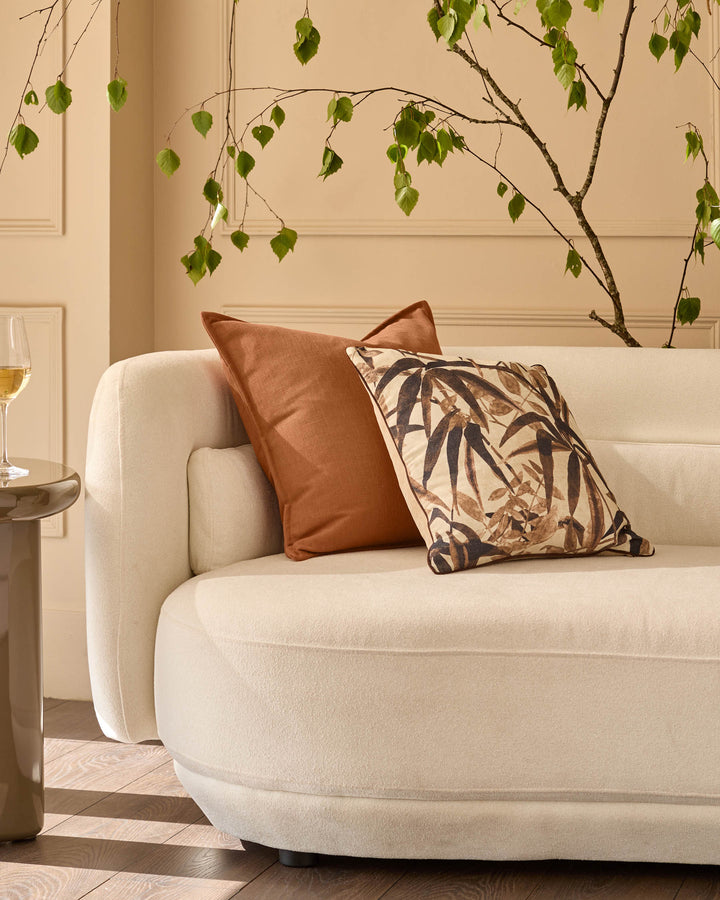 Large rust-colored cushion displayed on a cream upholstered armchair in a styled living room setting.