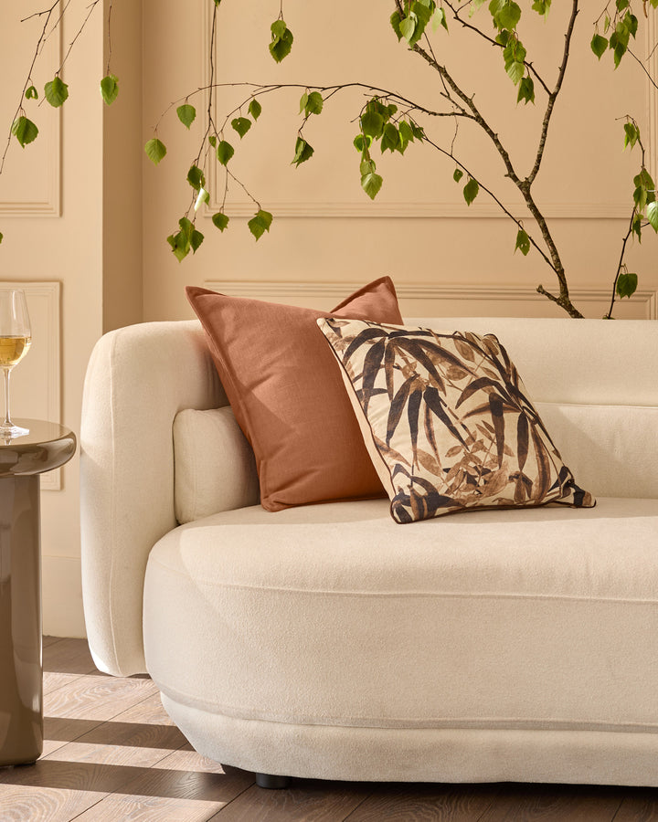 Madeira cushion in natural cream displayed on a beige armchair with decorative foliage backdrop.
