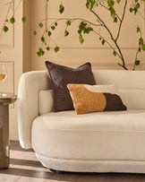 Large chocolate leather cushion displayed on a cream curved sofa in a styled living room setting.