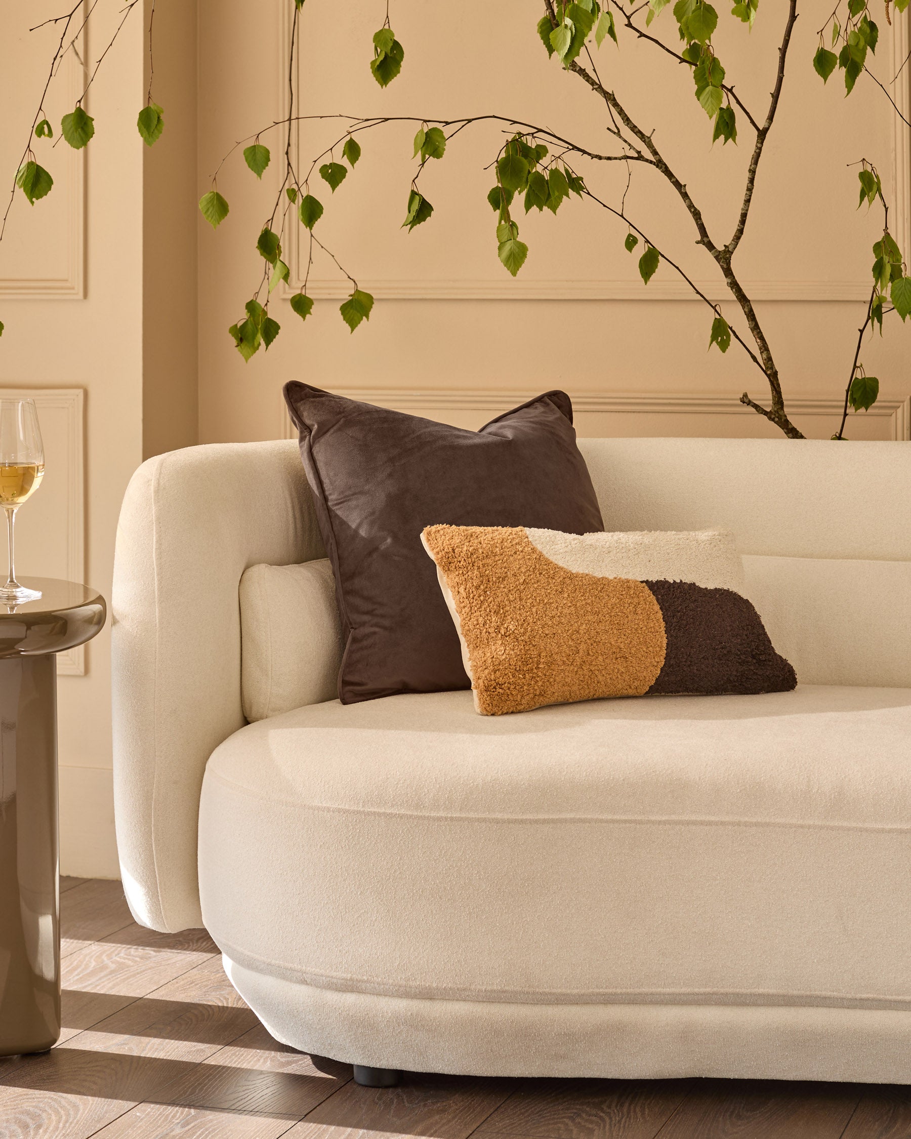 Large chocolate leather cushion displayed on a cream curved sofa in a styled living room setting.