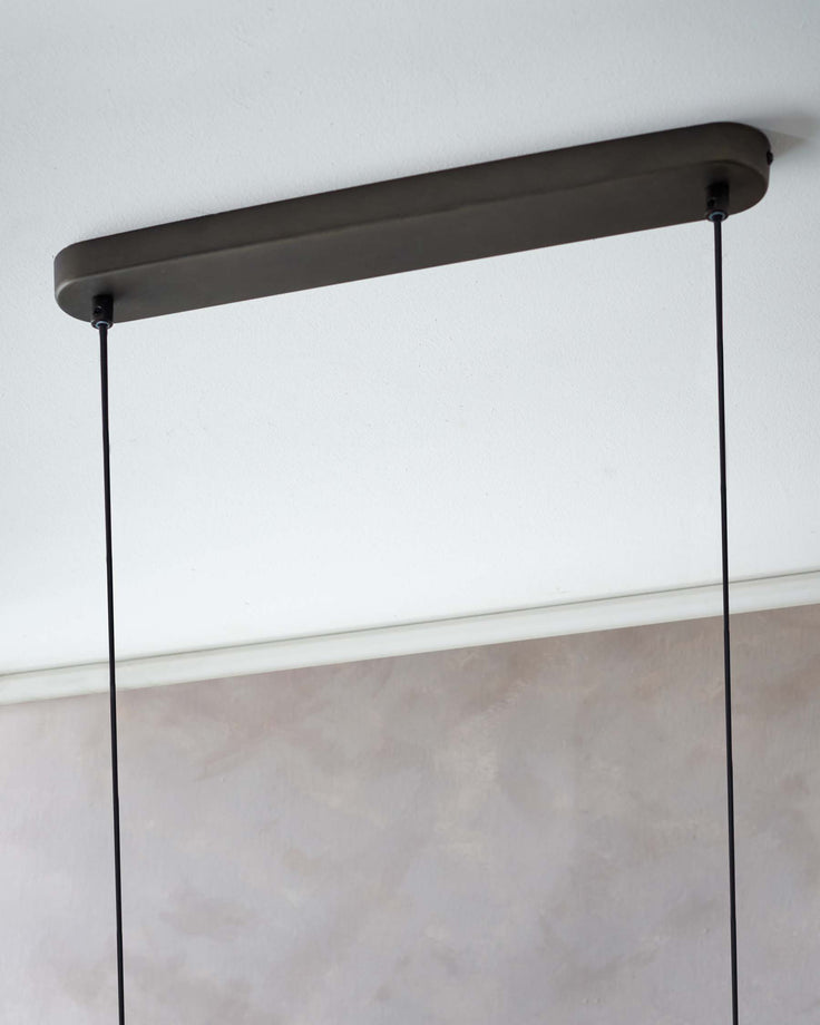 A close-up of a ceiling fixture. The fixture has a long, slim, dark bronze coloured bar, from which cords hang.