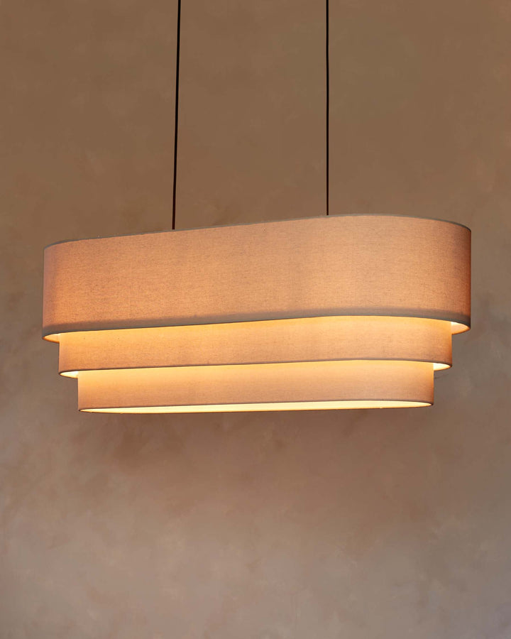 A layered, oblong ceiling light fixture suspended by two black cables against a neutral background.