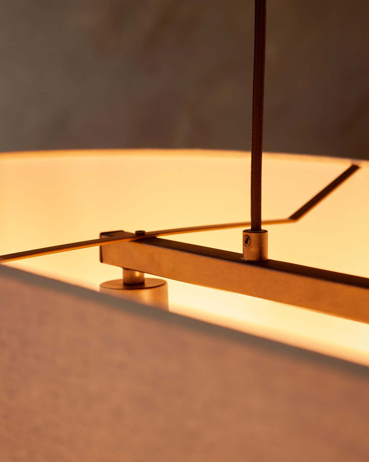 Close up on a modern light fitting with a brown cord and metal frame, emitting a warm light.