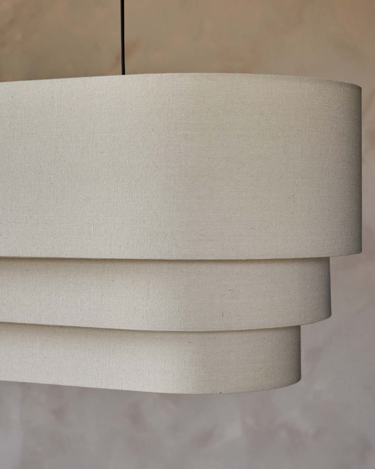 Beige tiered lampshade suspended by black cable. Neutral home decor lighting.