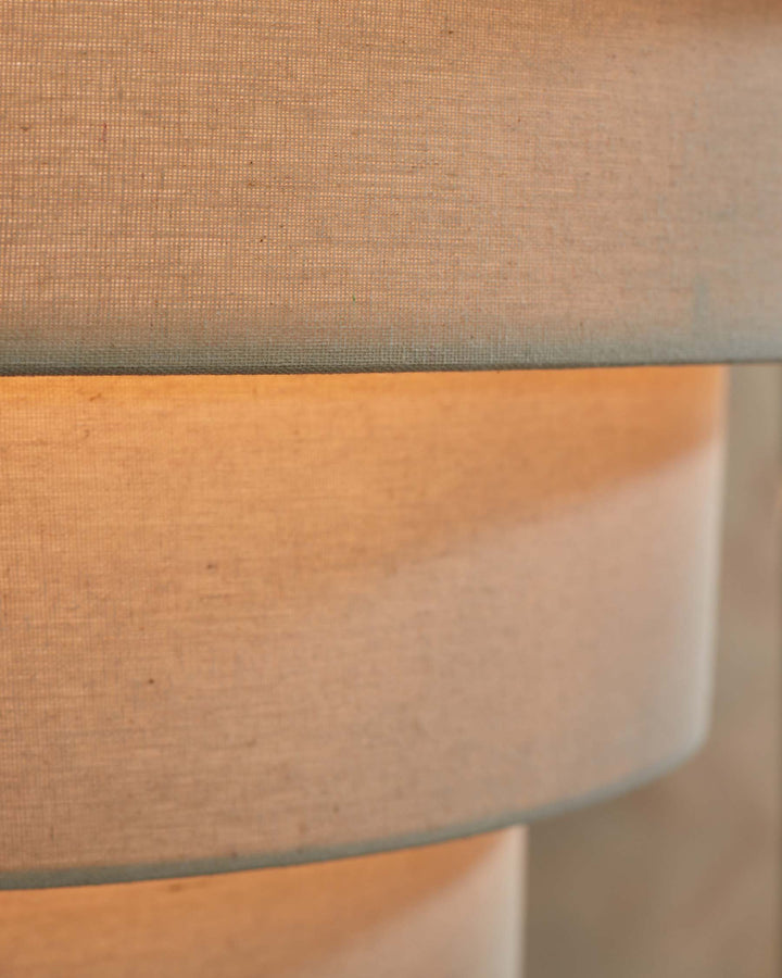 Close-up of a tiered lampshade, made from natural linen. The lamp is switched on, casting a warm glow.