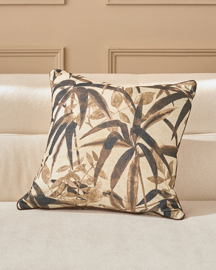 Madeira Cushion in natural tones featuring a botanical leaf pattern in charcoal and taupe on cream, displayed on a beige sofa.